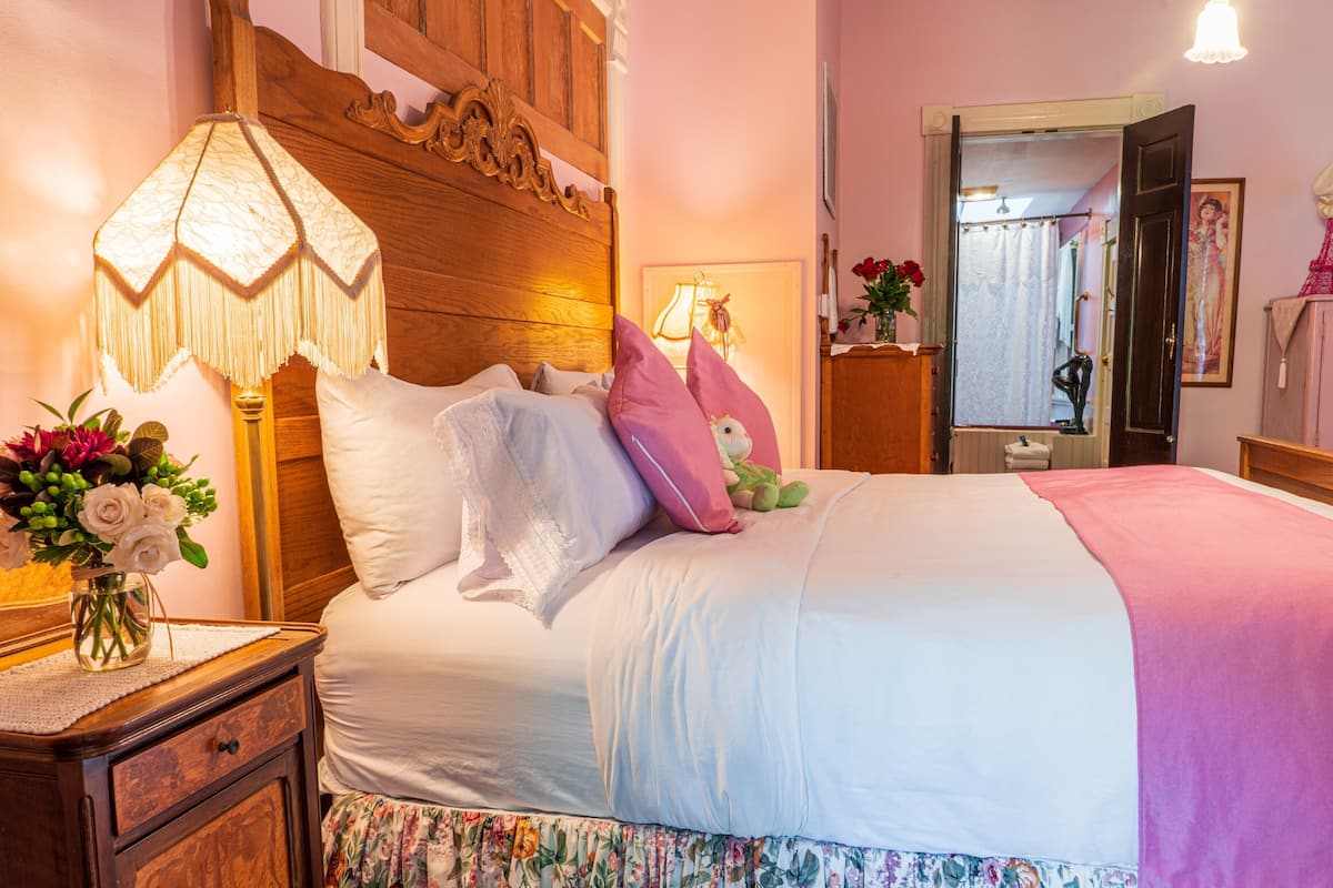 Una cama bien hecha con almohadas, una lámpara de noche y un arreglo floral en la mesita de noche.