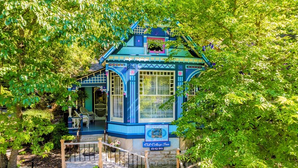Un pequeño edificio de estilo cabaña, azul, con un porche rodeado de abundante vegetación.