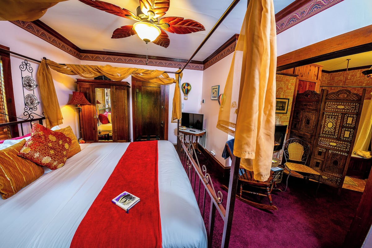 Una habitación con una cama, ventilador de techo, televisión y una silla.