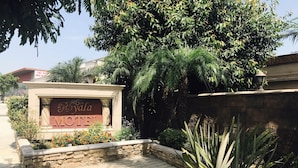 A hotel entrance with a sign reading "The Best ROYALA HOTEL" surrounded by lush greenery and a stone wall. - Royala Inn (Montebello)