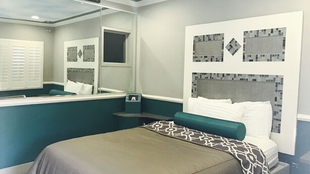 A hotel room with a bed, a mirror, a window with blinds, and a wall with a mosaic design. - Royala Inn (Montebello)