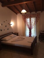 Un dormitorio con cama, mesita de noche, lámpara, ventana con cortinas y adhesivos decorativos de mariposas.
