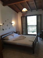 Quarto com cama de madeira, mesa de cabeceira, luminária na parede e janela com vista para o verde.