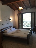 Un dormitorio con cama de madera, mesita de noche, lámpara de pared y ventana con vista a zonas verdes.