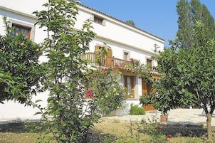 Um edifício branco com varanda, rodeado por vegetação e céu azul.
