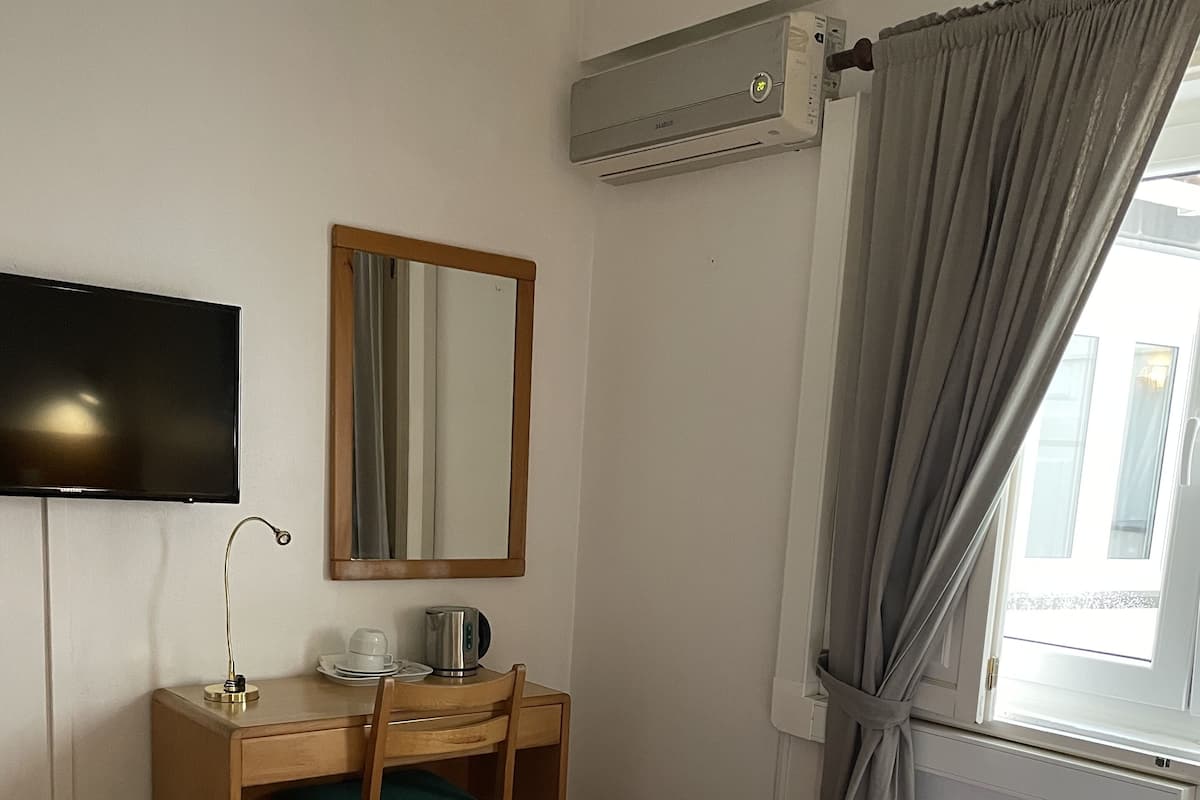 Ein Hotelzimmer mit einem Bett, einem Schreibtisch mit Stuhl, einem Fernseher und einer Klimaanlage.