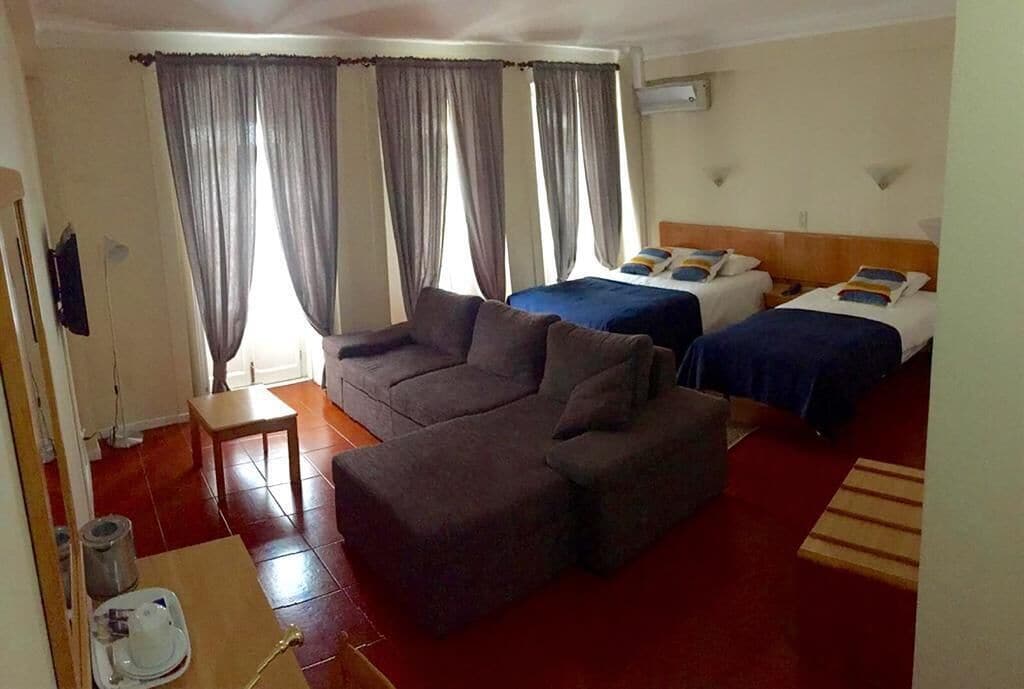 Habitación de hotel con sofá, dos camas, cortinas, una mesita y alfombra roja.