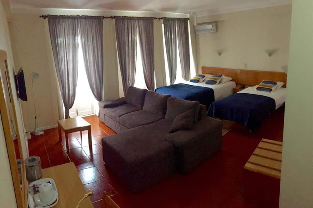 Ein Hotelzimmer mit einer Couch, zwei Betten, Vorhängen, einem kleinen Tisch und einem roten Teppich.