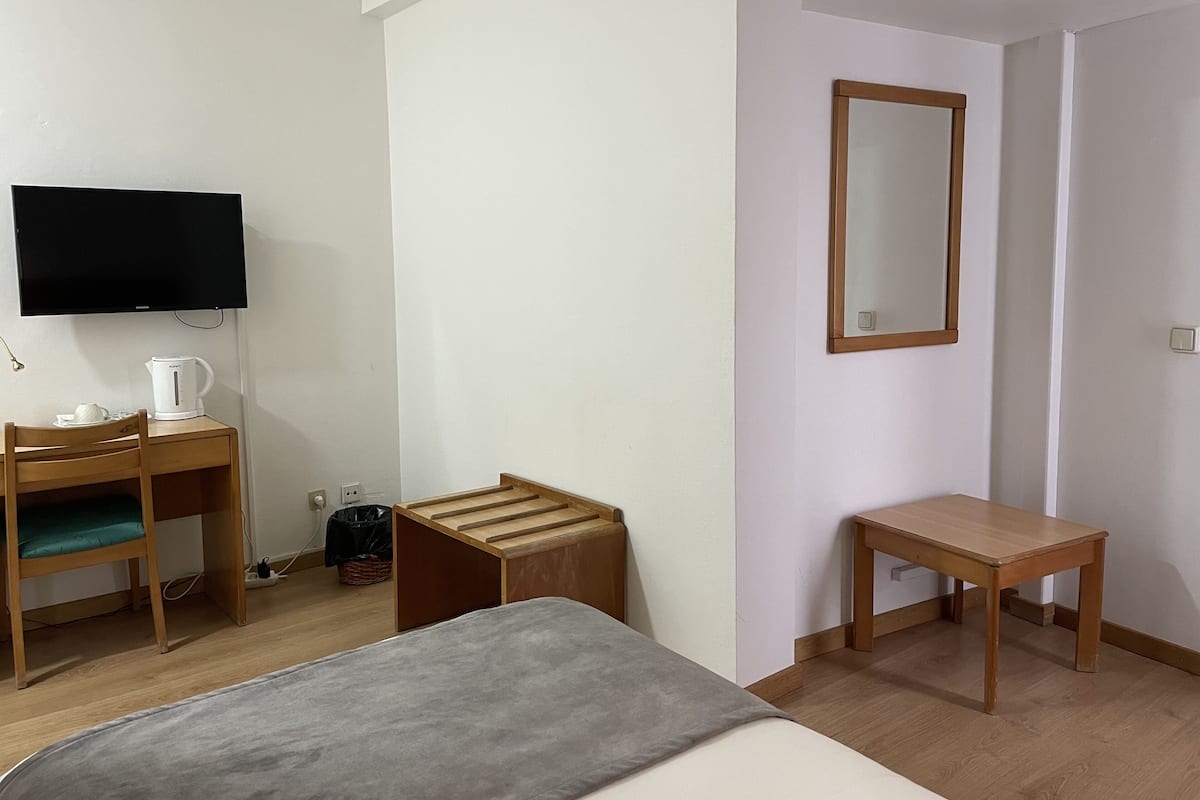 Ein Hotelzimmer mit einem Bett, einem Schreibtisch mit Stuhl, einem Fernseher und einem kleinen Holzschemel.