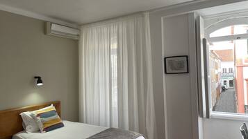 Una habitación de hotel con cama, mesita de noche, lámpara, ventana con cortinas y vista a la calle.