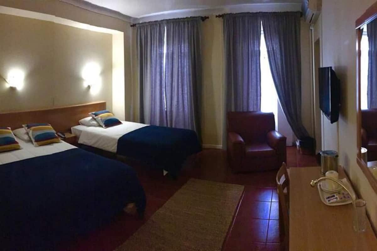 Ein Hotelzimmer mit zwei Betten, einem Sessel, einem Schreibtisch mit Telefon und einem Spiegel.