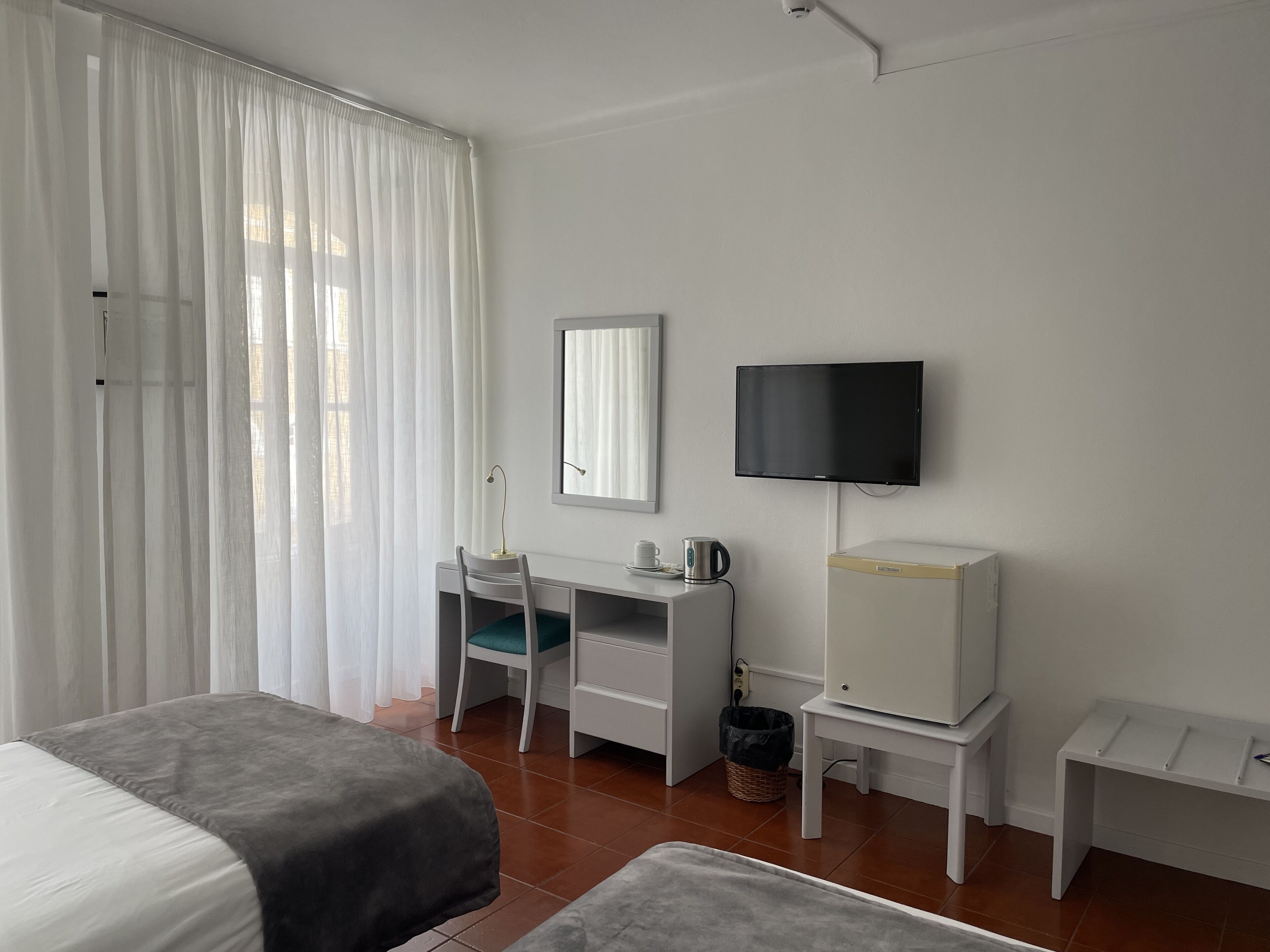 Een hotelkamer met een bed, een bureau met stoel, een televisie en een klein tafeltje.