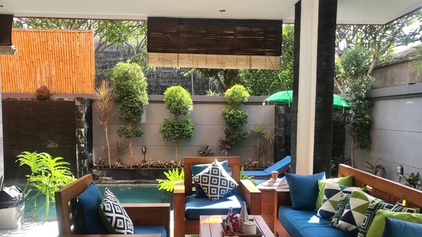 A modern outdoor living space with a pool, wooden furniture, and lush greenery. - Villa Legian (Legian)