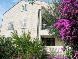 A two-story building with a balcony, surrounded by lush greenery and purple flowers. - Apartments Ivica (Dubrovnik)