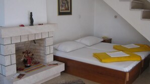 A bedroom with a fireplace, a bed with yellow blankets, a staircase, and a framed picture on the wall. - Apartments Ivica (Dubrovnik)