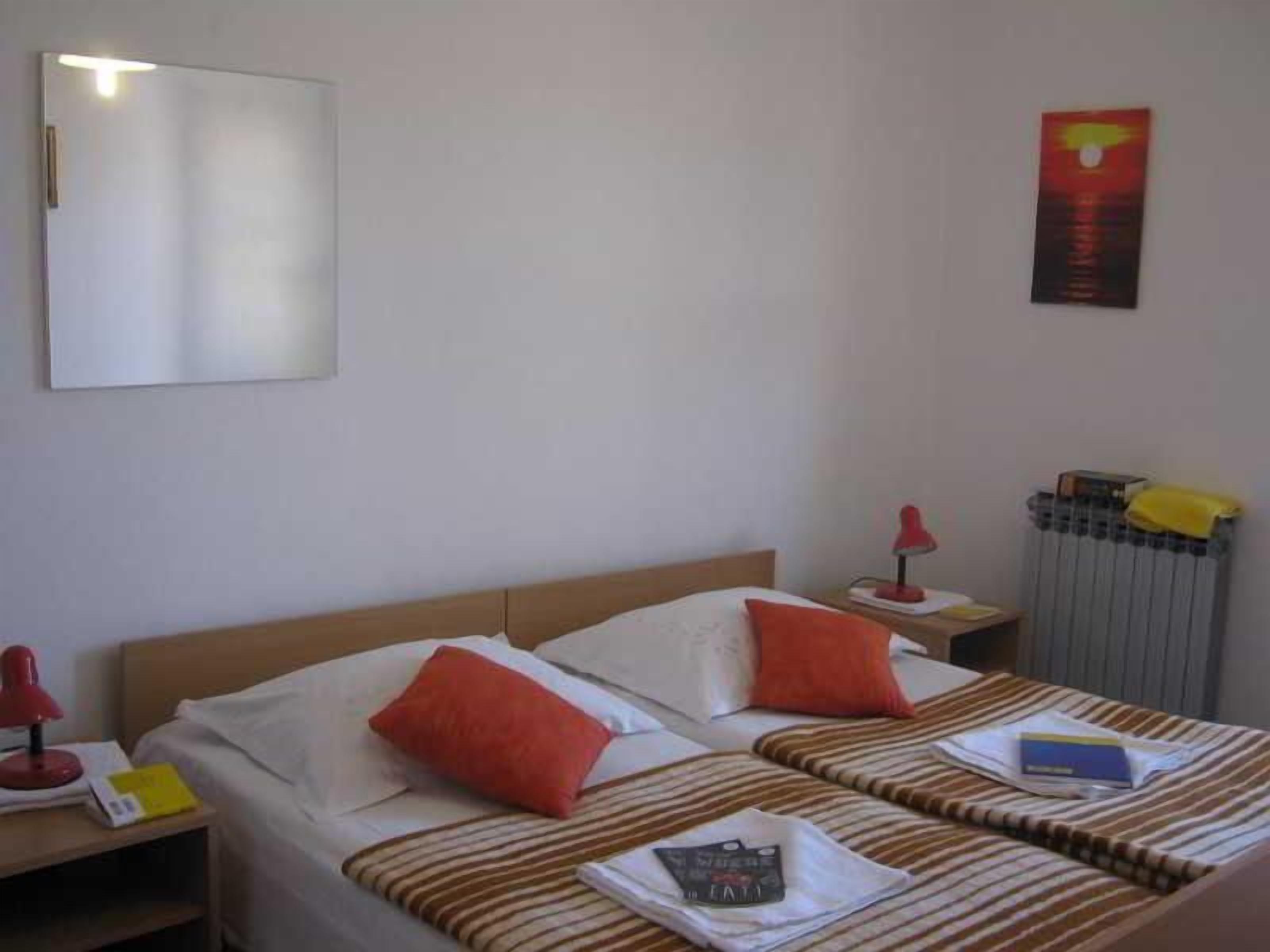 A hotel room with two beds, a mirror, a radiator, and a red lamp.