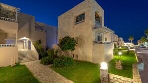 A modern building with a stone facade, a staircase leading to a balcony, and a well-lit entrance. - Erato Beach Hotel (Platanias)