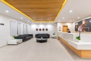 A modern reception area with a wooden reception desk, two grey sofas, a coffee table, and a reception counter. - Erato Beach Hotel (Platanias)