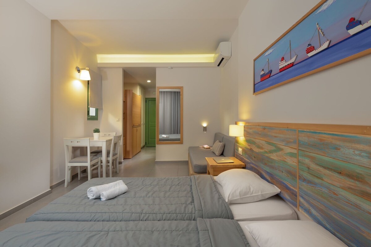 A hotel room with two beds, a desk, a chair, a painting, and a view of the corridor.