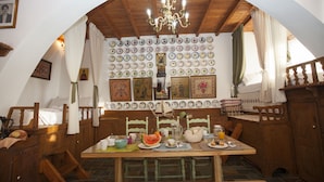 Un comedor con una mesa de madera, sillas y una araña. Hay platos y una jarra sobre la mesa.