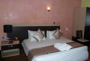 Une chambre d’hôtel avec un grand lit, une table de chevet avec une lampe, un téléphone et une petite table sur laquelle se trouvent un livre et une bouteille.