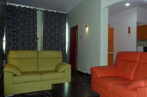 Une pièce avec un canapé jaune et un fauteuil orange, une moquette à motifs et une porte avec un interrupteur.