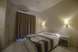 A hotel room with a bed, bedside lamps, a nightstand, and an air conditioning unit.