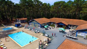 Un área de piscina con varias piscinas, sillas de descanso y un patio cubierto con mesas y sombrillas.