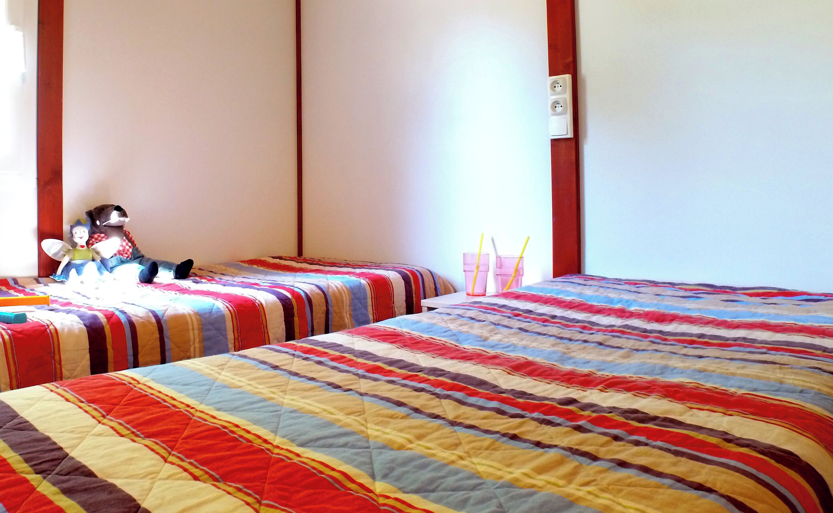 Ein Schlafzimmer mit zwei Betten, gestreifter Bettwäsche, einem Nachttisch, einer Lampe und einem Stofftier.