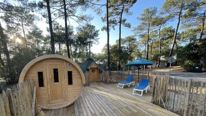 Una terraza de madera con sillones de descanso y una pequeña construcción de madera.
