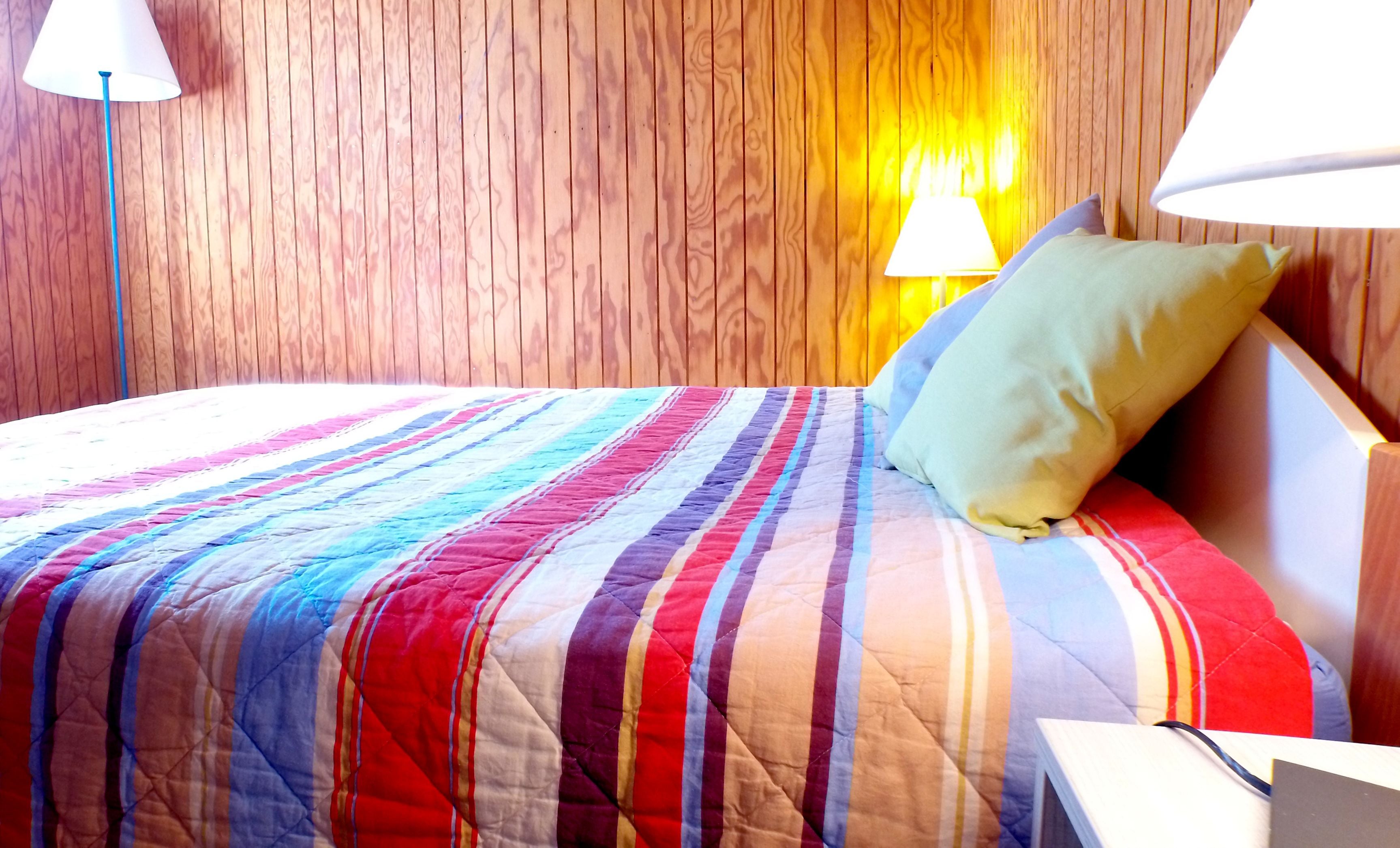 A bed with a colorful striped quilt, a pillow, and a nightstand with a lamp.