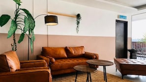 Una sala moderna con un sofá de cuero marrón, una mesita redonda y una planta verde grande.