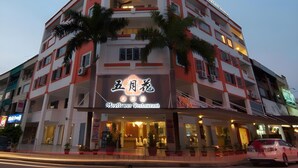 Un hotel de varios pisos con una fachada llamativa anaranjada y blanca, un restaurante visible llamado 'Mayflower Restaurant' y varias balcones con plantas.