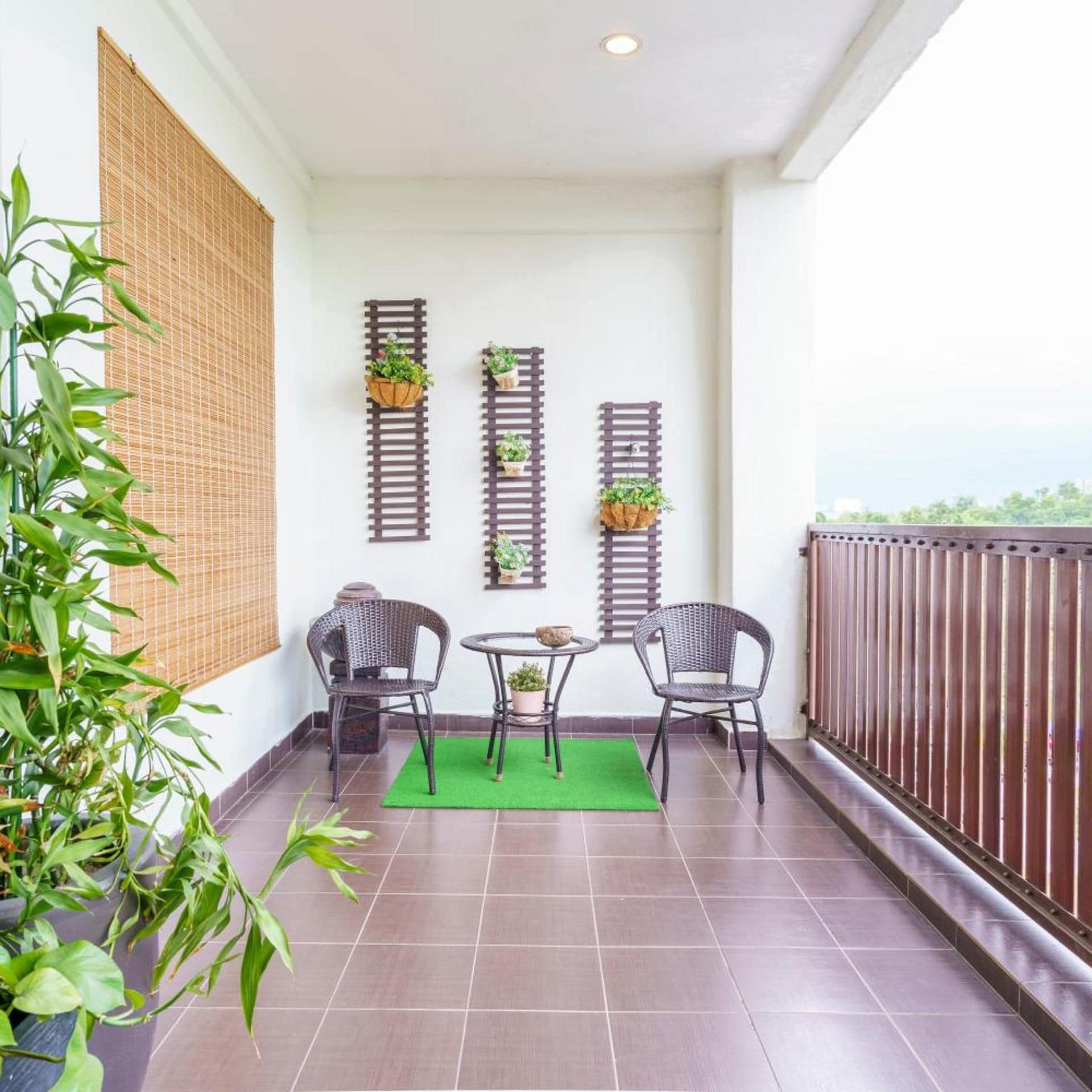 A balcony with two wicker chairs, a small round table, and potted plants on wall-mounted shelves.