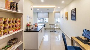 Una habitación de hotel con kitchenette, un comedor con mesa y sillas, un escritorio con teclado y monitor, y estantes llenos de aperitivos.