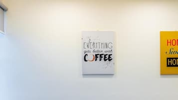 A room with a round table and four chairs, a white wall with two framed signs, one reading 'EVERYTHING gets better with COFFEE' and the other partially visible.