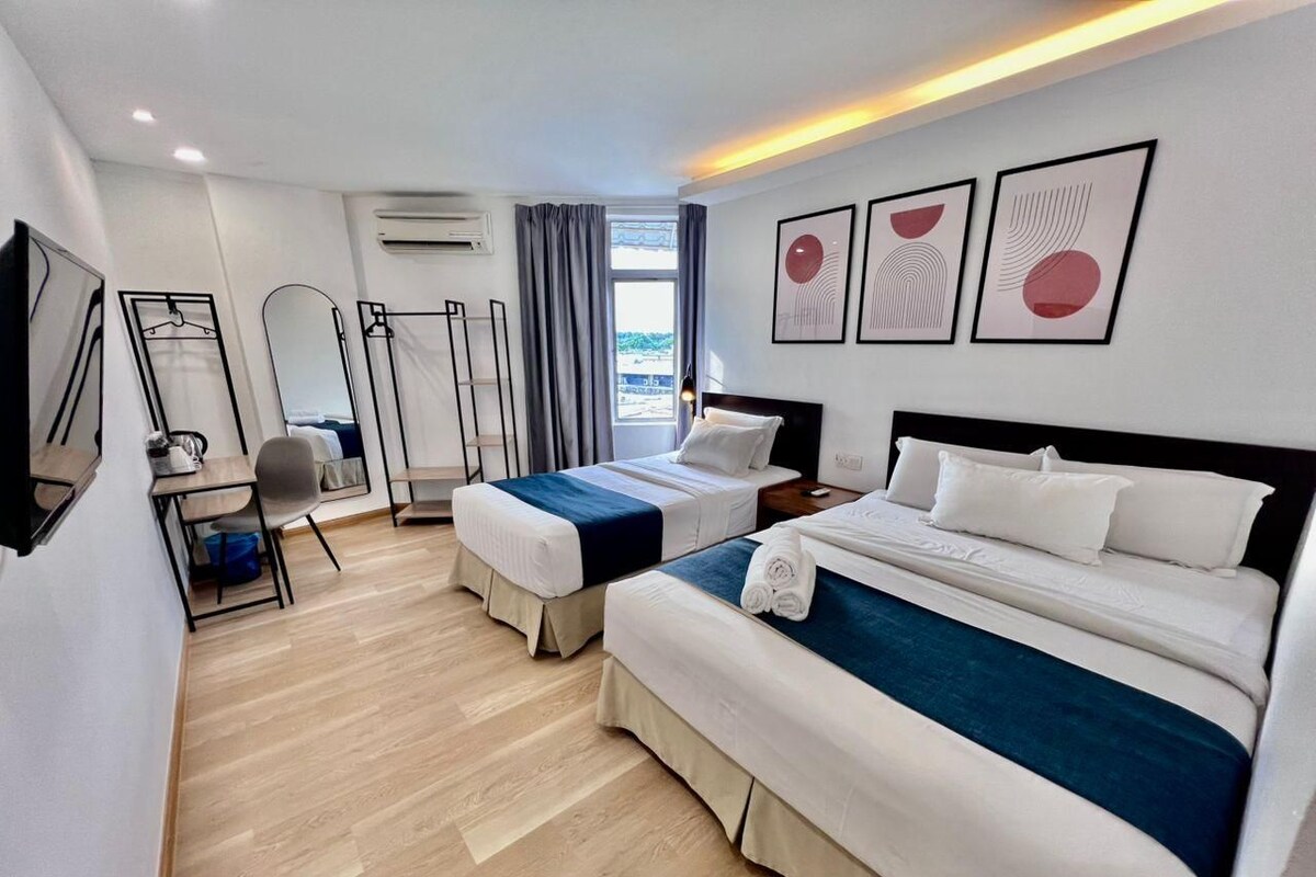A hotel room with two beds, a desk, a chair, and artwork on the wall.