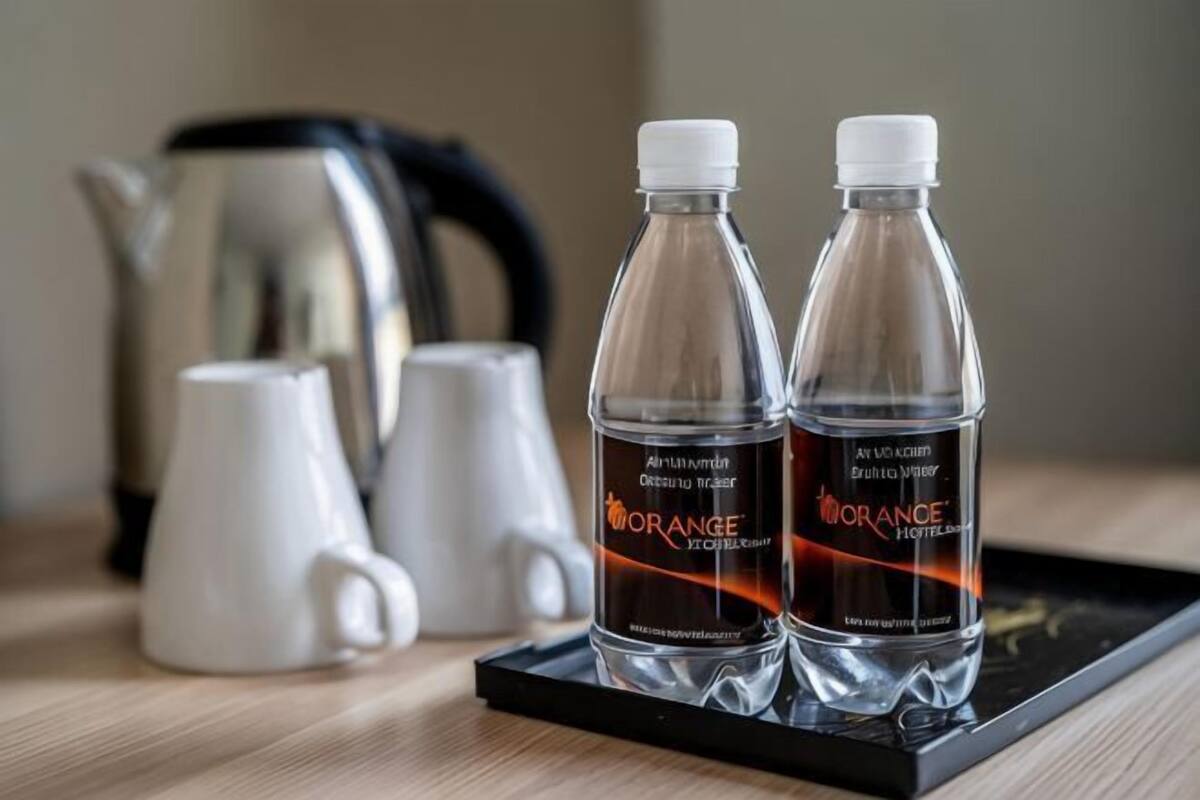 Two bottles of orange juice and two white mugs on a tray.