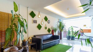 Un vestíbulo moderno con sofá de cuero negro, césped artificial verde, plantas en macetas y elementos decorativos en la pared.