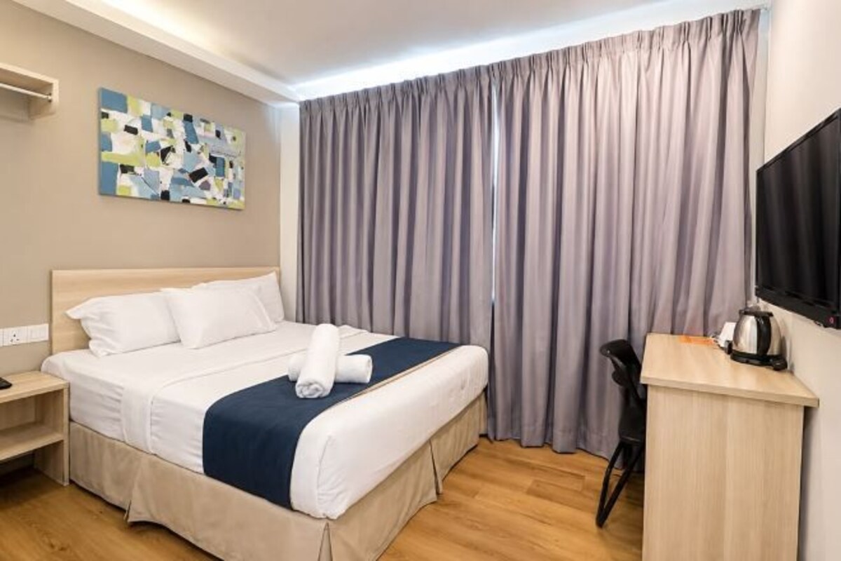A hotel room with a bed, a desk, a chair, a television, and a painting on the wall.