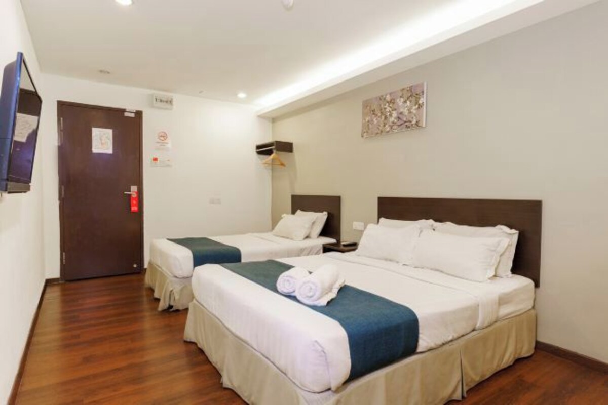 A hotel room with two beds, a wooden floor, a flat-screen TV, and a painting on the wall.