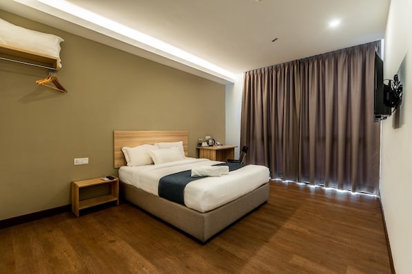 Una habitación de hotel con cama, mesita de noche y televisor montado en la pared.