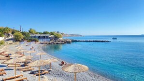 A beach with sun loungers and umbrellas, a building with a blue roof, and a clear blue sea. - Ariadne Beach (Hersonissos)