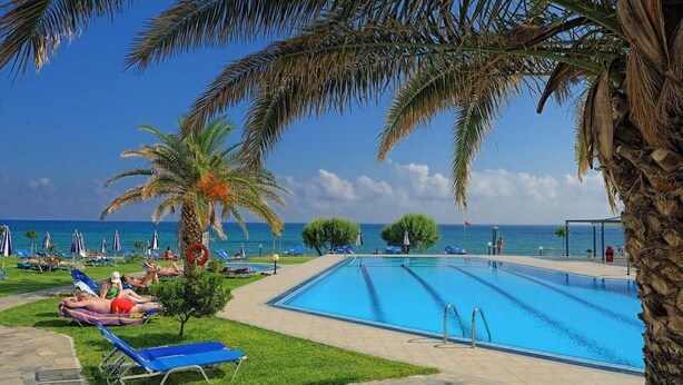 A swimming pool with lounge chairs and palm trees, overlooking a beach. - Ariadne Beach (Hersonissos)