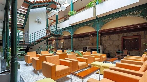 A spacious lobby with a central staircase, multiple seating areas, and a stone wall. - Universal (Terras de Bouro)