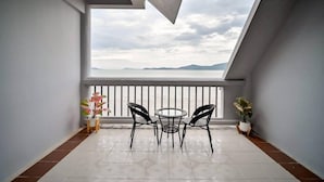 A balcony with a view of the sea, a round table, two chairs, and potted plants.