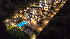 Una casa moderna de varios pisos con piscina, mobiliario exterior y caminos bien iluminados.