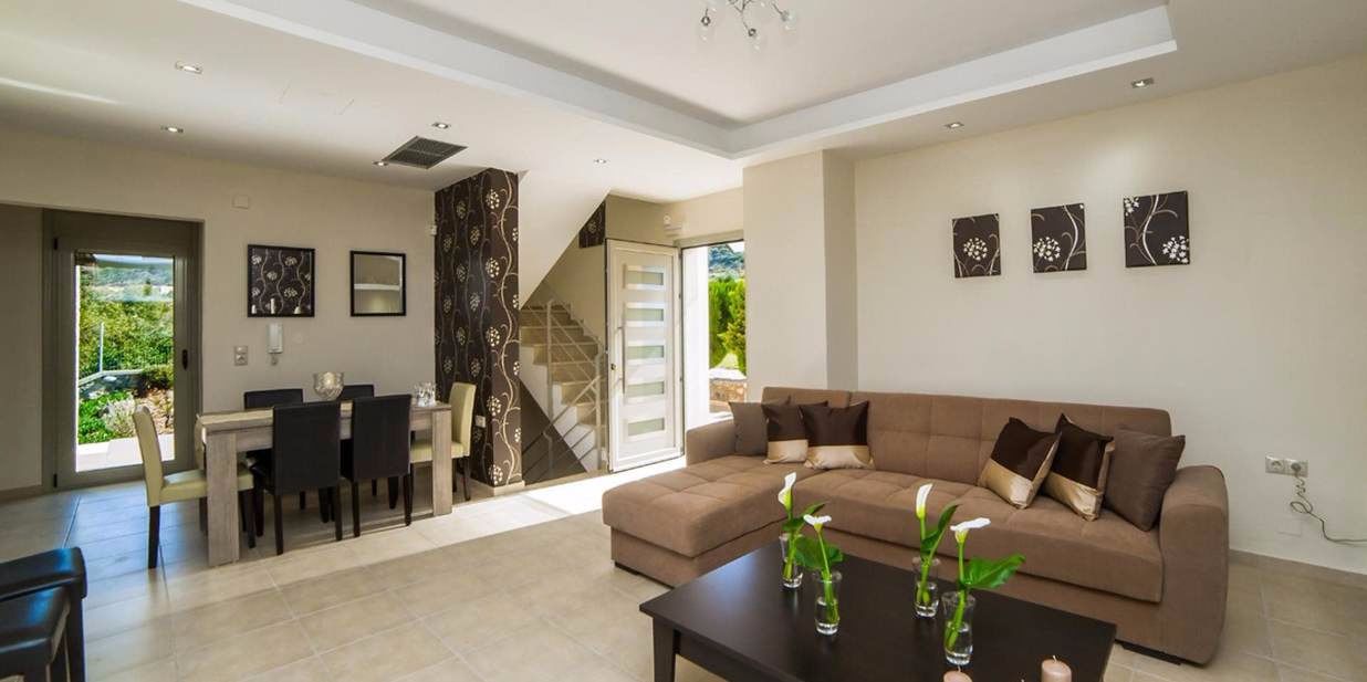A modern living room with a brown sofa, a dining table with chairs, and a staircase leading to an upper floor.