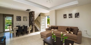 Una sala de estar moderna con un sofá marrón, una mesa de comedor con sillas y una escalera que lleva a un piso superior.