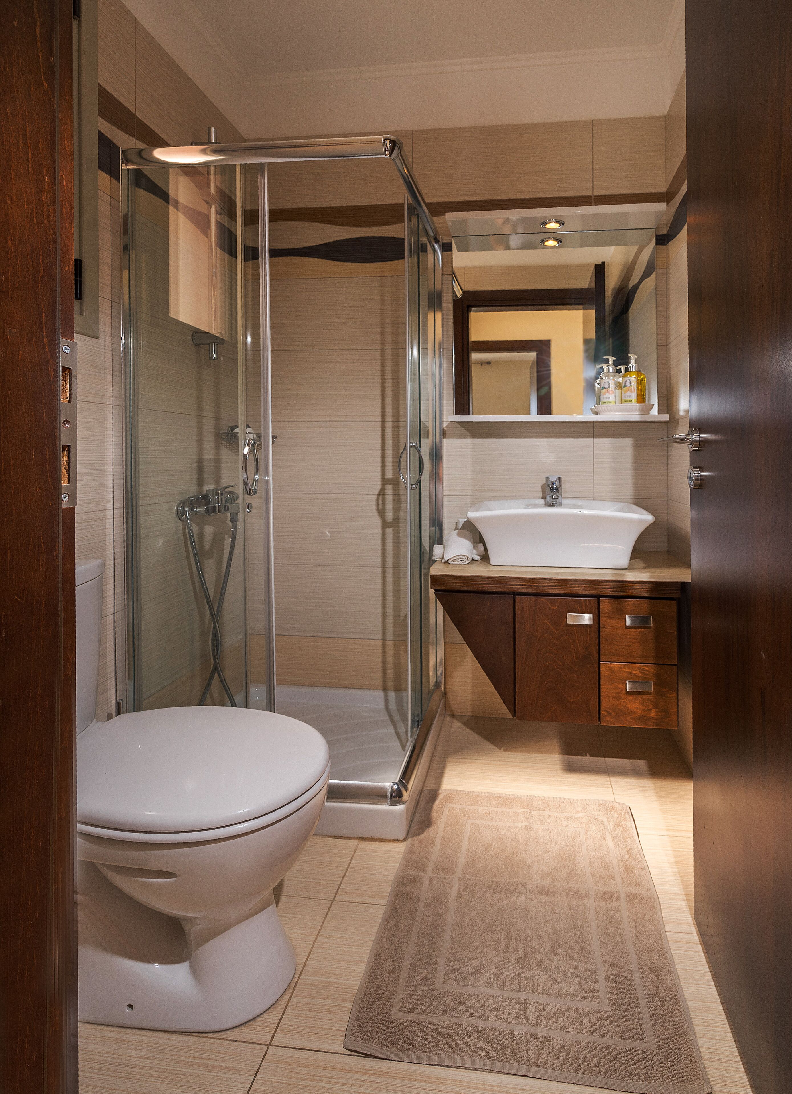A modern bathroom with a glass-enclosed shower, a white toilet, a sink, and wooden cabinetry.